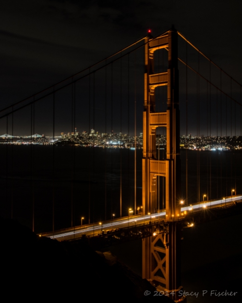 Golden Gate north tower at night, with city lights of San Francisco and Bay Bridge in the distance